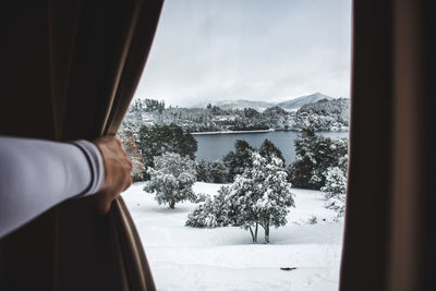 Cropped hand of person looking through window during winter