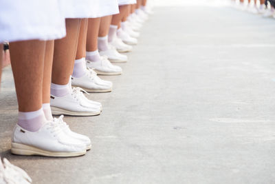 Low section of women wearing white shoes standing in row on road