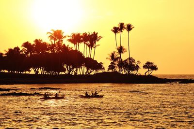 Silhouette people sailing boats in sea against palm trees during sunset