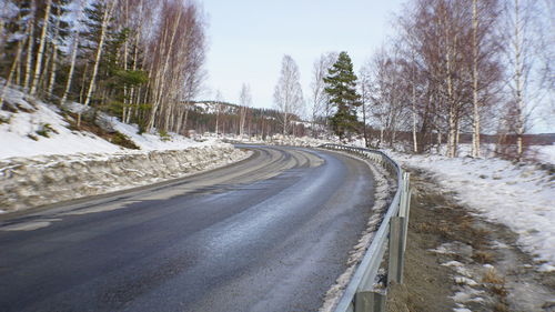 Snow covered road amidst trees against sky