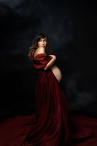 Rear view of pregnant woman staying against black background with red dress