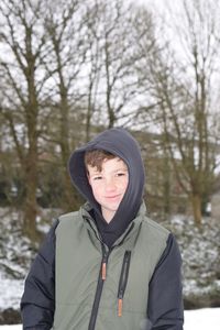 Portrait of boy in warm clothing standing against bare trees