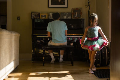 A little girl in tutu dances in living room while father plays piano