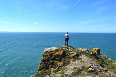 Rear view of mature woman looking at sea while standing on mountain against blue sky