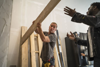 Multiracial male carpenters carrying plank while working in apartment