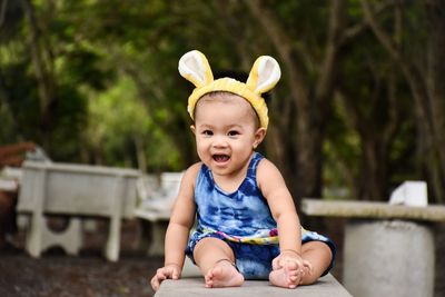 Portrait of cheerful baby girl wearing headband while sitting on railing