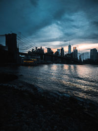 Sea by buildings against sky at dusk