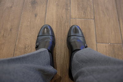 Low section of man wearing black leather shoes on hardwood floor