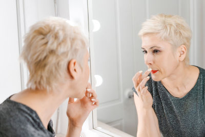 Beautiful woman with short haircut looking in mirror at her home.