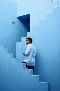 Young latin man holds his cell phone in a blue building