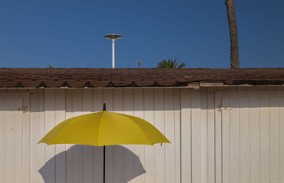 Yellow umbrella against white wooden building with blue clear sky