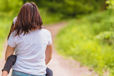 Rear view of woman carrying daughter while standing at park