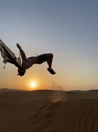 Man jumping in desert against sky during sunset