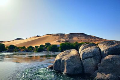 Rocks by river against clear blue sky