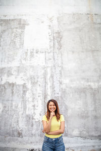 Portrait of a smiling young woman standing against wall