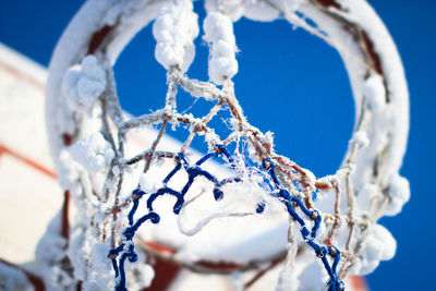 Low angle view of frozen basketball hoop against blue sky during winter