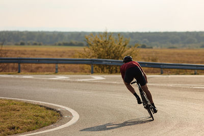 Young sportsman in protective helmet cycling with high speed on paved road. morning sun