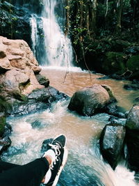 Low section of person standing on rocks by river