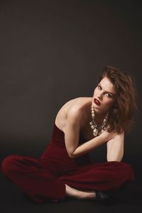 Portrait of beautiful young woman sitting against black background