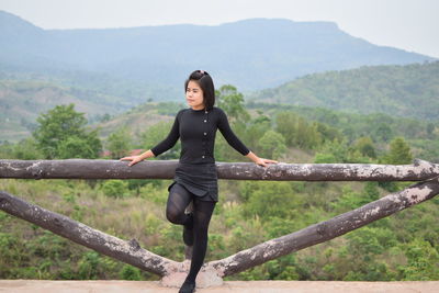 Young woman looking away while standing by railing on observation point against mountain