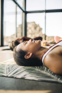 Smiling female instructor lying on exercise mat while doing yoga at retreat center