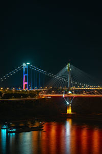 Illuminated bridge over river in city at night