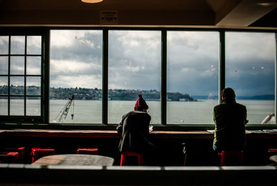 Rear view of people sitting in cafe by sea against cloudy sky