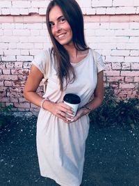 Portrait of smiling young woman standing against brick wall