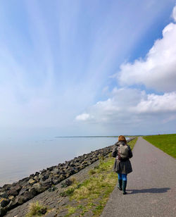 Rear view of woman with umbrella on sea against sky