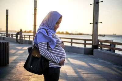 Woman walking on footpath by railing against sky