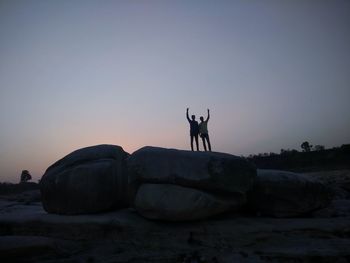 Silhouette people standing on rock against sky during sunset