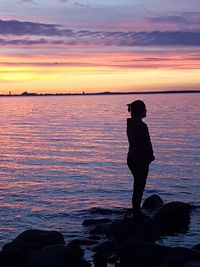 Silhouette man photographing sea against sky during sunset