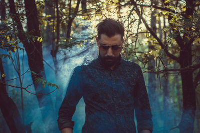 Young man standing by trees in forest