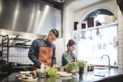 Young male chef preparing food by female colleague at kitchen counter in restaurant