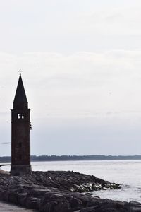 Lighthouse by sea against sky