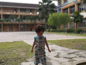 Cute boy standing on footpath against building