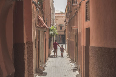 Rear view of people walking on narrow alley amidst buildings