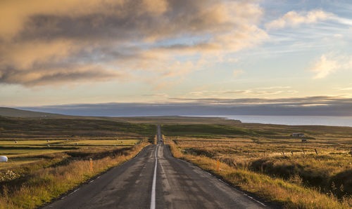 Road amidst field against sky during sunset