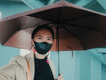 Portrait of woman wearing mask while holding umbrella