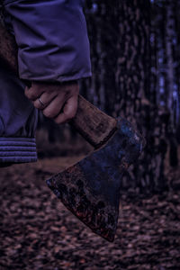 Cropped image of woman holding axe in forest