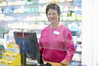 Happy pharmacist seen through glass at pharmacy