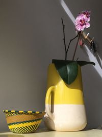 Close-up of yellow flower in vase on table against wall