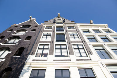 Low angle view of tall canal houses in amsterdam against clear blue sky