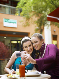 Cheerful female friends taking selfie while sitting at outdoor cafe