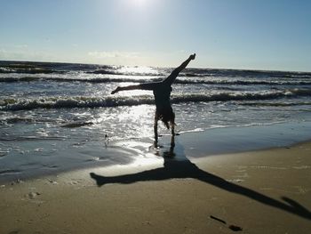 Silhouette woman doing handstand on wet shore