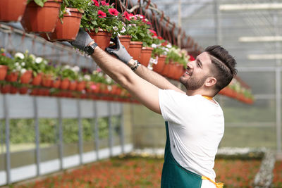 Side view of young man holding flower in greenhouse