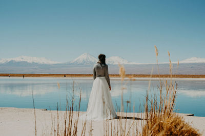 Rear view of woman standing by lake against sky