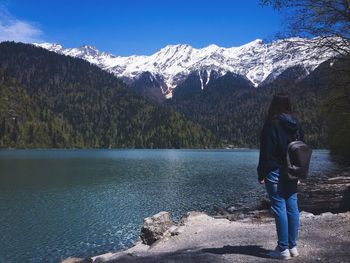 Full length of woman with backpack looking at lake by mountains during winter