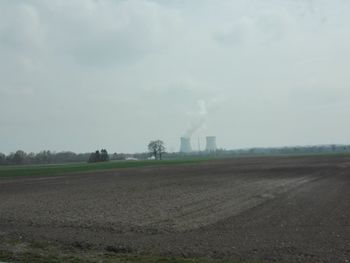 Field by factory against sky