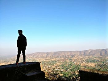 Man standing on rock against clear blue sky